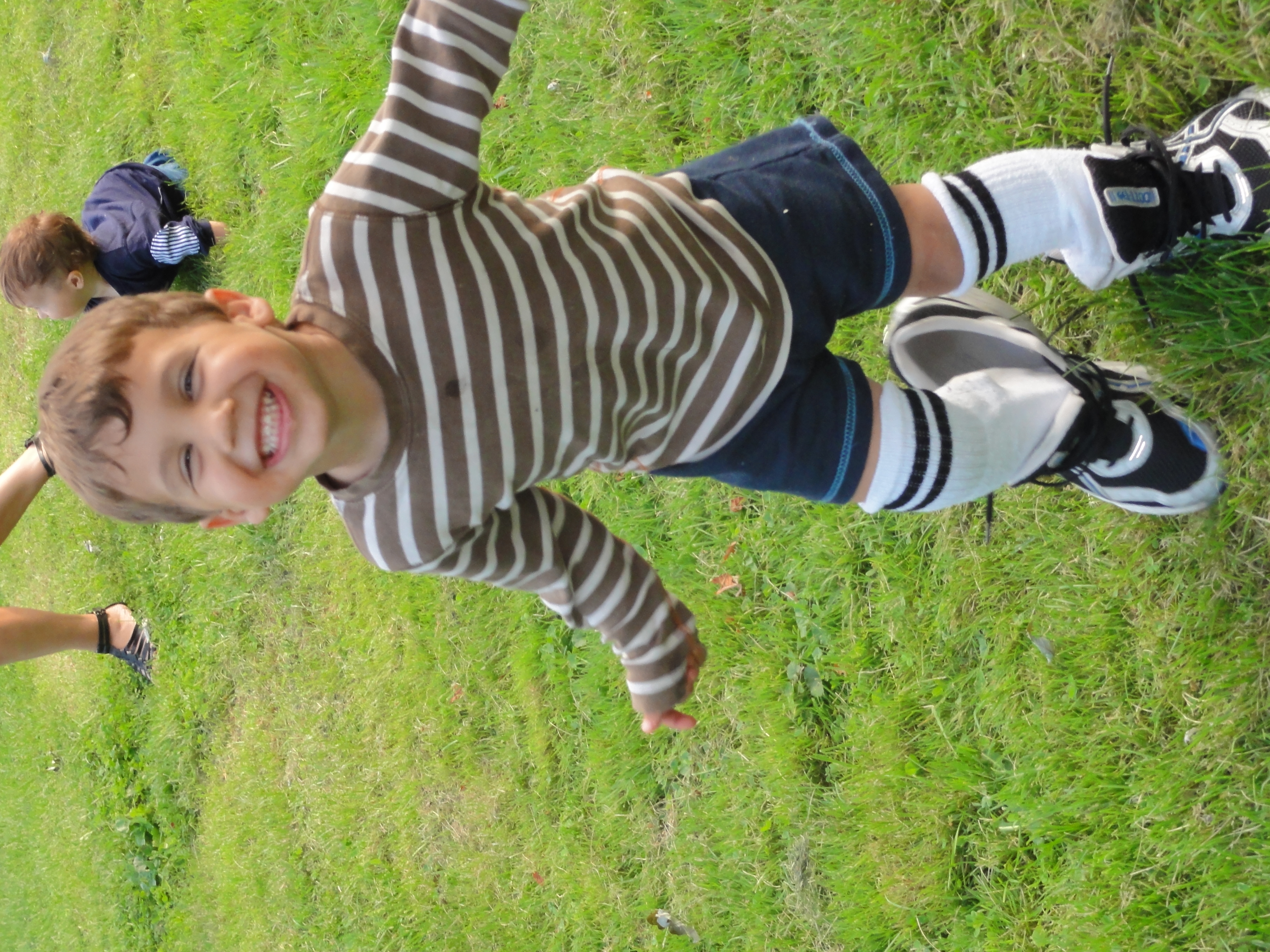 Young boy smiling while wearing his father’s shoes, symbolizing walking in his dad’s footsteps and learning through love.