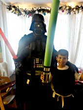 Darth vader in costume with red lightsaber in hand with Birthday boy in homemade Jedi knight robe and Star Wars pool noodle sword